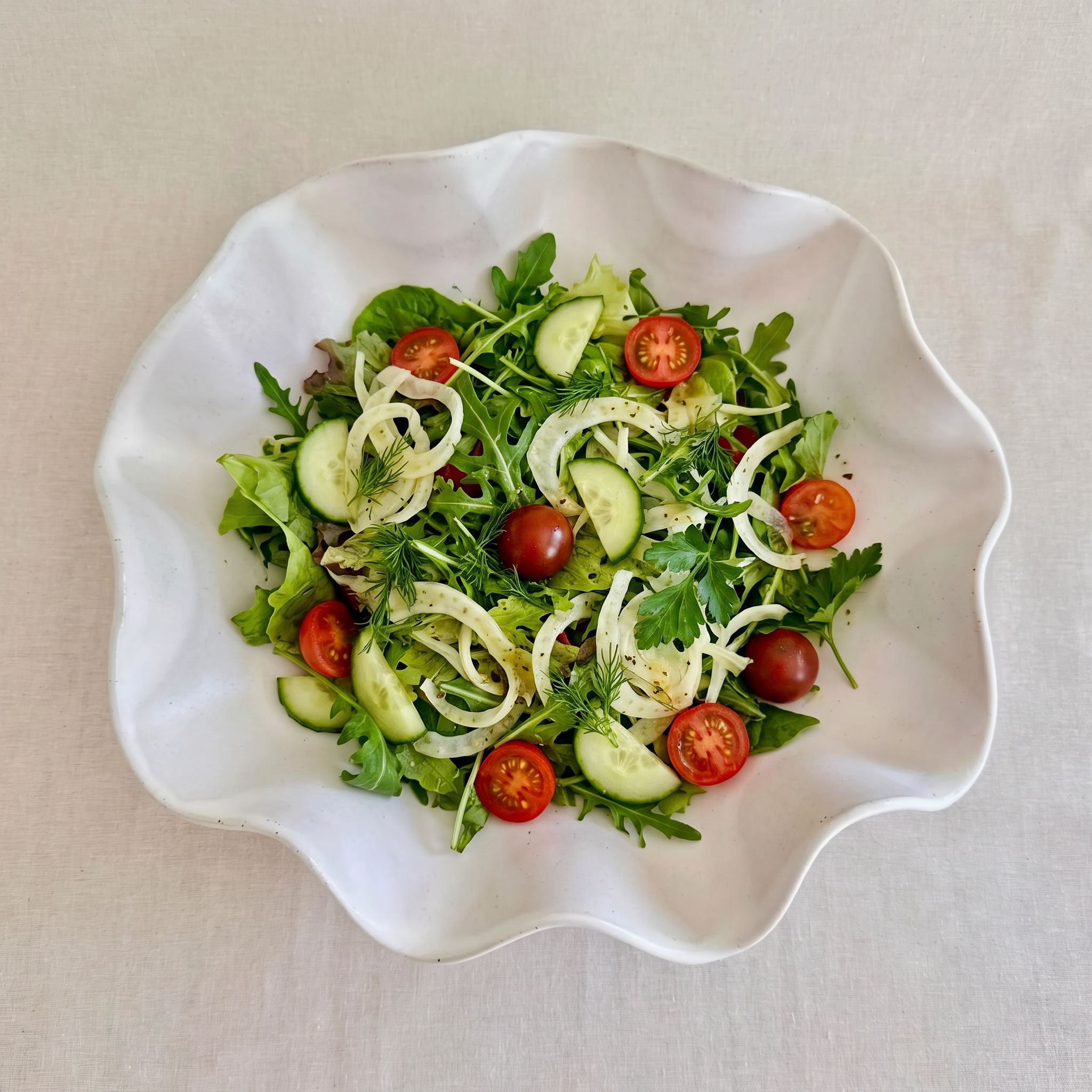 A wavy white handmade bowl filled with fresh salad